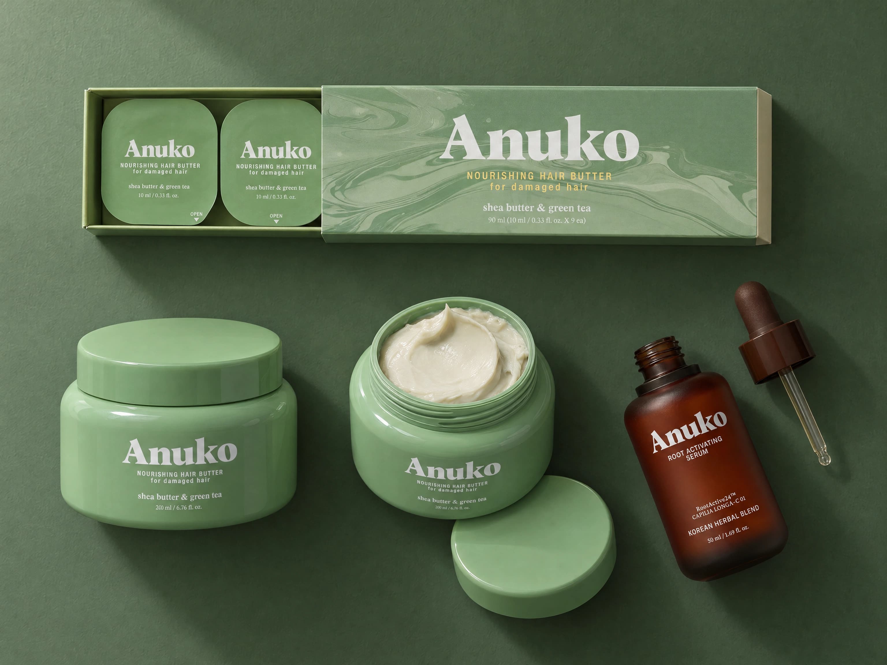 The Anuko routine: Hair Butter jar, open jar, Travel carton and Root Activating Serum on a deep sage ground