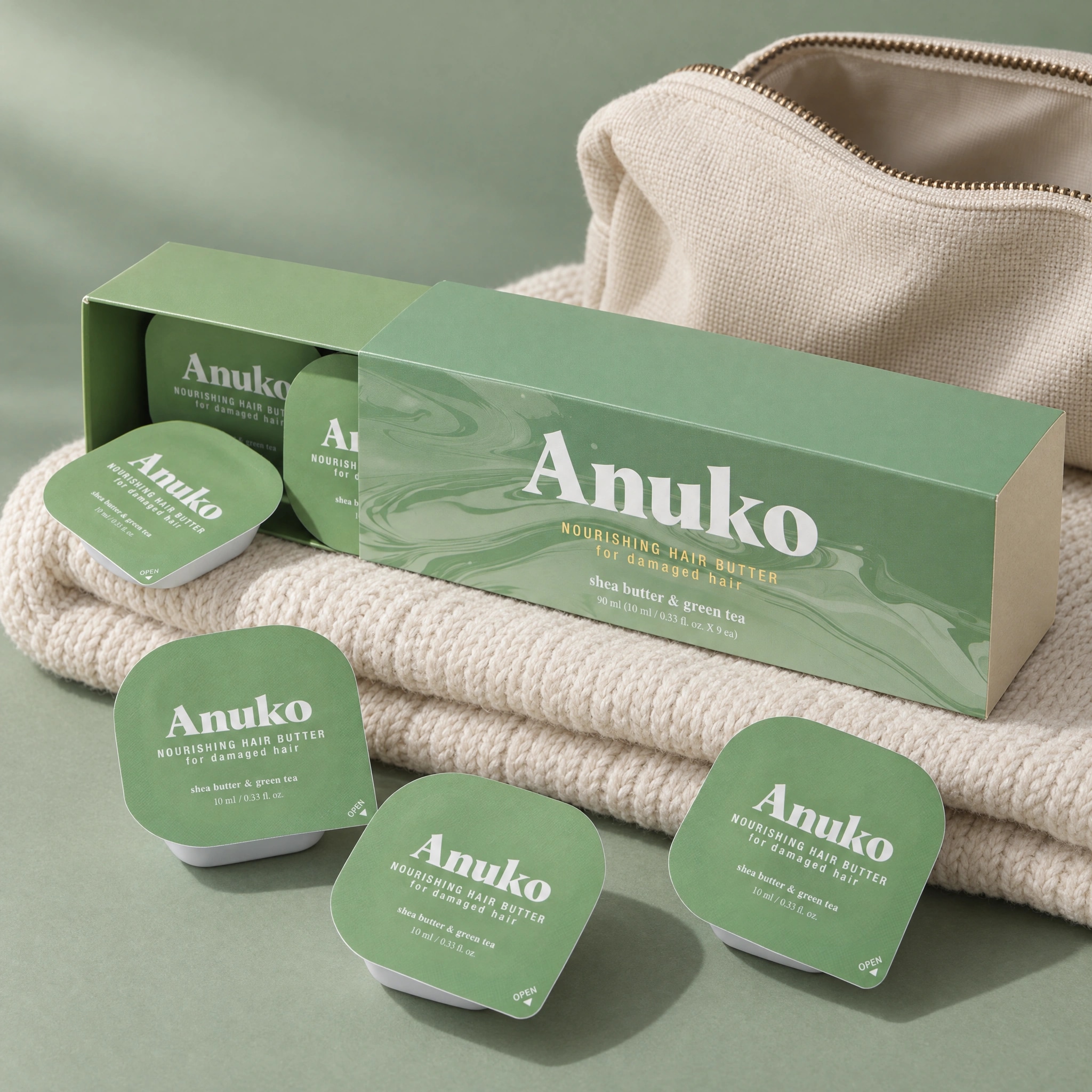 Anuko Travel Hair Butter carton and sachets resting on a folded sweater beside a travel pouch
